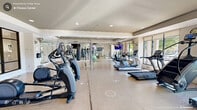 This fitness center in Durham, NC is a generously sized, single-floor facility designed to accommodate a full range of workout activities. The open floor plan is thoughtfully organized into distinct training zones, creating an efficient and welcoming environment for all fitness levels.

The cardio zone features a row of treadmills, elliptical trainers, and stair climbers, all positioned along large floor-to-ceiling windows that invite abundant natural light and provide views of the surrounding outdoor greenery. Mounted flat-screen televisions throughout the space enhance the workout experience.

The strength training area is well-appointed with a comprehensive dumbbell rack, weight benches, cable machines, and a multi-function strength machine, all set against large wall mirrors that visually expand the space and allow users to monitor their form.

A dedicated functional training zone houses a freestanding suspension training rig complete with TRX straps and a heavy punching bag, offering versatile options for dynamic and bodyweight-based workouts. Stability balls and additional accessories are neatly stored nearby.

The interior finishes are clean and modern, featuring light-toned flooring, recessed lighting, and a tray ceiling detail that adds architectural interest. The overall ambiance is bright, spacious, and professionally designed, making this fitness center a comprehensive destination for health and wellness.