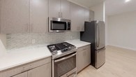 This single-floor unit offers a thoughtfully designed layout with modern finishes and practical amenities. The open living area features light hardwood flooring, recessed lighting, and a sliding glass door that leads to a balcony, filling the space with natural light. Neutral walls create a clean, versatile backdrop throughout.

The kitchen is well-appointed with taupe-toned cabinetry extending to the ceiling, white quartz countertops, a geometric mosaic tile backsplash, and a full suite of stainless steel appliances, including a gas range, over-the-range microwave, and French door refrigerator. Light hardwood flooring continues seamlessly from the living area into the kitchen.

The bedroom features plush carpeting, a double-door closet, and a window that allows natural light. The bathroom is finished with a light wood-grain vanity, white quartz countertop, a large mirror with overhead lighting, a medicine cabinet, and a tiled tub-shower combination with floor-to-ceiling vertical tile surround. Light tile flooring completes the space.

A dedicated laundry closet with louvered doors houses a full-size washer and dryer with overhead shelving, providing added convenience within the unit.