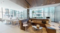 Located at 1326 S Michigan Ave in Chicago's South Loop, this sophisticated single-floor amenity lounge exemplifies contemporary design with a refined, hospitality-inspired aesthetic. The space is defined by expansive floor-to-ceiling glass walls that flood the interior with natural light and frame views of a landscaped outdoor terrace and the surrounding cityscape.

The main lounge area features a striking slatted wood ceiling that adds warmth and texture, contrasting beautifully with the light large-format tile flooring. Plush L-shaped sectional seating in earthy tones anchors the central gathering area, complemented by sleek glass-top coffee tables and modern accent chairs arranged across layered area rugs. A dedicated dining and co-working zone offers clean white tables with contemporary chairs, supported by built-in shelving displaying curated décor.

A sunlit lounge nook along the glass perimeter showcases swivel lounge chairs paired with pedestal side tables, creating an ideal setting for relaxed conversation or quiet reflection. Rich wood-paneled walls and columns provide architectural contrast throughout.

Enclosed glass-walled private meeting pods, fitted with herringbone wood flooring, pendant lighting, and intimate seating, offer focused work or conferencing options. The seamless indoor-outdoor connection, abundant natural light, and thoughtfully layered furnishings combine to create a versatile, upscale communal environment.