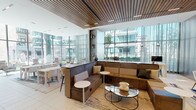 Located at 1326 S Michigan Ave in Chicago's South Loop, this sophisticated single-floor amenity lounge exemplifies contemporary design with a refined, hospitality-inspired aesthetic. The space is defined by expansive floor-to-ceiling glass walls that flood the interior with natural light and frame views of a landscaped outdoor terrace and the surrounding cityscape.

The main lounge area features a striking slatted wood ceiling that adds warmth and texture, contrasting beautifully with the light large-format tile flooring. Plush L-shaped sectional seating in earthy tones anchors the central gathering area, complemented by sleek glass-top coffee tables and modern accent chairs arranged across layered area rugs. A dedicated dining and co-working zone offers clean white tables with contemporary chairs, supported by built-in shelving displaying curated décor.

A sunlit lounge nook along the glass perimeter showcases swivel lounge chairs paired with pedestal side tables, creating an ideal setting for relaxed conversation or quiet reflection. Rich wood-paneled walls and columns provide architectural contrast throughout.

Enclosed glass-walled private meeting pods, fitted with herringbone wood flooring, pendant lighting, and intimate seating, offer focused work or conferencing options. The seamless indoor-outdoor connection, abundant natural light, and thoughtfully layered furnishings combine to create a versatile, upscale communal environment.