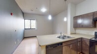 Located at 1307 Hayes St in La Crosse, Wisconsin, this single-floor unit offers a well-organized layout designed for comfortable everyday living. The kitchen is a functional centerpiece, outfitted with dark espresso cabinetry, a double-basin stainless steel sink, a Whirlpool electric range, a full-size refrigerator, a built-in dishwasher, and a range hood. Pendant lighting hangs above the extended counter peninsula, which opens directly into the adjacent living and dining area. This connected space features warm light hardwood flooring and a window that frames views of mature surrounding trees, filling the area with natural light. Two bedrooms are finished with plush carpeting and neutral wall tones, each receiving natural light through windows overlooking the wooded surroundings — providing a calm, comfortable atmosphere. The full bathroom is generously proportioned, featuring tile flooring, a large vanity with dark wood cabinetry and a wide mirror, and accessible grab bars along the walls. Throughout the unit, clean white walls, dark baseboards, and consistent finishes create a cohesive and understated aesthetic. The overall layout is practical and efficient, making effective use of the available space across each room.