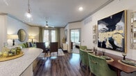 This single-story residence offers a thoughtfully designed open-concept layout connecting the living, dining, and kitchen areas in a seamless flow. Dark hardwood-style flooring runs through the main living spaces, complemented by crown molding and neutral wall tones that create a polished, cohesive aesthetic. Ceiling fans are installed throughout, adding both function and a finished look to each room.

The kitchen is outfitted with rich dark cabinetry, stainless steel appliances, granite countertops, a subway tile backsplash, and an island that provides additional prep and counter space. The dining area accommodates a full-sized table and benefits from its open sightlines to the living space.

Multiple bedrooms are present, each featuring plush carpet, large windows that invite natural light and outdoor views, and ceiling fans. One bedroom connects directly to a well-appointed bathroom featuring dark cabinetry, dual sinks with granite countertops, hardwood-style flooring, and a soaking tub with white tile surround. A second bathroom mirrors this refined style with similar cabinetry and finishes. The overall ambiance of the residence is modern and sophisticated, with consistent design elements tying each space together.