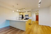 Located at 2702 Hoyt Ave in Everett, WA, this 1-bedroom, 1-bathroom unit offers a well-designed open-concept layout with modern finishes throughout. Light-toned hardwood flooring flows seamlessly across the entire space, contributing to a bright and cohesive aesthetic.

The combined living, dining, and kitchen area forms the heart of the unit. The kitchen is equipped with stainless steel appliances, including a refrigerator, electric range, microwave, and dishwasher. Light wood cabinetry with clean lines provides ample storage, while a spacious kitchen island with a built-in sink and light blue-grey countertop serves as both a functional workspace and a casual dining spot. Pendant lighting above the island and track lighting across the ceiling add layered illumination to the space.

The living area benefits from large sliding glass doors that invite abundant natural light and offer views of surrounding greenery, creating a seamless connection to the outdoors. A hallway with built-in storage leads to the private bedroom and bathroom. The bedroom is a comfortable, well-proportioned retreat. The bathroom features a full tub-shower combination, a wood-toned vanity with a light countertop, and clean white walls. The unit is accessed through a distinctive red entry door visible from the main living area.