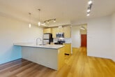 Located at 2702 Hoyt Ave in Everett, WA, this 1-bedroom, 1-bathroom unit offers a well-designed open-concept layout with modern finishes throughout. Light-toned hardwood flooring flows seamlessly across the entire space, contributing to a bright and cohesive aesthetic.

The combined living, dining, and kitchen area forms the heart of the unit. The kitchen is equipped with stainless steel appliances, including a refrigerator, electric range, microwave, and dishwasher. Light wood cabinetry with clean lines provides ample storage, while a spacious kitchen island with a built-in sink and light blue-grey countertop serves as both a functional workspace and a casual dining spot. Pendant lighting above the island and track lighting across the ceiling add layered illumination to the space.

The living area benefits from large sliding glass doors that invite abundant natural light and offer views of surrounding greenery, creating a seamless connection to the outdoors. A hallway with built-in storage leads to the private bedroom and bathroom. The bedroom is a comfortable, well-proportioned retreat. The bathroom features a full tub-shower combination, a wood-toned vanity with a light countertop, and clean white walls. The unit is accessed through a distinctive red entry door visible from the main living area.