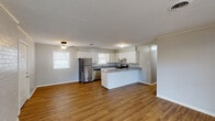 Located in Ingleside, TX, this single-story home offers a well-designed layout with consistent warm-toned hardwood-style flooring running throughout every room. The open-concept living and kitchen area serves as the heart of the home, providing a spacious, airy feel enhanced by natural light from multiple windows with blinds. A painted brick accent wall in the living room adds a distinctive architectural character to the space.

The kitchen is thoughtfully appointed with crisp white cabinetry extending to the ceiling for ample storage, granite countertops with subtle gray and white veining, and a full suite of stainless steel appliances including a refrigerator, range, and dishwasher. A peninsula provides additional counter space and reinforces the open flow between the kitchen and living areas.

The bedrooms are well-sized with neutral gray walls, textured ceilings, and continued hardwood-style flooring. At least one bedroom features a generous closet with dual hanging rods, offering practical storage capacity. The bathroom includes a tub and shower combination surrounded by elegant marble-look tile, adding a refined touch. Throughout the home, clean white trim and neutral finishes create a cohesive, move-in-ready atmosphere.