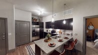 Located at 950 FM-156 in Justin, TX, this single-floor residence offers a thoughtfully designed layout with modern finishes and a cohesive aesthetic throughout. The kitchen is a standout feature, showcasing rich dark cabinetry that extends to the ceiling, granite countertops, a classic white subway tile backsplash, and a full suite of stainless steel appliances including a French door refrigerator, electric range, and built-in microwave. A large kitchen island with granite surfaces and bar seating serves as a natural gathering point, illuminated by elegant pendant lighting. Wood-look flooring flows through the kitchen and living areas, adding warmth and continuity. The living room is bright and inviting, accented by a bold warm-toned feature wall, ceiling fan, and natural light from multiple windows. The bedroom continues the warm accent wall design, complete with plush carpet, a ceiling fan, and a window with blinds and curtains. A second bedroom offers neutral tones, carpet flooring, and natural light. The bathroom includes a full tub and shower combination with clean, neutral finishes and wood-look flooring. Throughout the space, stylish gray interior doors and cohesive design elements tie the rooms together for a polished, contemporary feel.