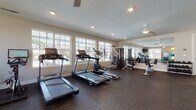 Located at 1733 Bellmeadow Dr in Lancaster, Ohio, this single-floor fitness center is thoughtfully designed to support a comprehensive workout experience. The space is outfitted with durable rubber flooring throughout, providing both safety and comfort during exercise. Recessed lighting and ceiling fans ensure the room remains well-lit and ventilated, while an abundance of large, multi-pane windows along the walls floods the space with natural light and offers views of the surrounding exterior.

The cardio zone features multiple treadmills, an elliptical trainer, a stationary spin bike, and a rowing machine, catering to a wide range of cardiovascular workouts. A wall-mounted flat-screen television is positioned for easy viewing during cardio sessions. The strength training area includes a multi-station cable machine, an adjustable weight bench, and a well-stocked dumbbell rack. A large floor-to-ceiling mirror visually expands the space while allowing users to monitor their form.

Rounding out the amenities is a dedicated accessory station with medicine balls, stability balls, resistance bands, and yoga mats. French doors with glass panels connect the fitness area to an adjacent space, adding an open and airy feel to the overall layout. The textured ceiling and neutral wall tones contribute to a clean, functional ambiance throughout.