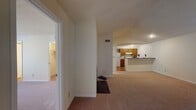 This single-floor residence at 910 Constitution Dr in Durham, NC offers a well-organized layout with a variety of functional living spaces. The living room is a standout area, featuring vaulted ceilings that lend a sense of openness and volume, soft wall-to-wall carpeting, and a large multi-pane window that frames views of surrounding greenery and an outdoor balcony, filling the space with natural light. The kitchen is efficiently designed in a galley style, equipped with warm-toned wood cabinetry, gray laminate countertops, white appliances including a stove and dishwasher, and hardwood flooring. A peninsula counter connects the kitchen to the adjacent dining or living area, providing additional workspace and a casual serving surface. The bedrooms are carpeted and well-proportioned, each benefiting from natural light through generous windows. A walk-in closet is accessible from one of the bedrooms, adding practical storage. The bathrooms feature hardwood flooring, vanities with wood cabinetry, and shower-tub combinations. Throughout the home, neutral tones and clean white trim create a consistent, understated aesthetic that lends itself well to personalization.