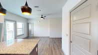 This thoughtfully designed single-floor residence offers a functional and modern layout across five distinct spaces: a kitchen, living room, bedroom, bathroom, and closet. The open-concept kitchen is a standout feature, showcasing rich dark-stained cabinetry, granite countertops, a white subway tile backsplash, and a full suite of stainless steel appliances including a range, microwave, and refrigerator. A central island with a granite surface and stylish pendant lighting anchors the kitchen and flows seamlessly into the living area, which features warm wood-look flooring and a ceiling fan. The living space is bright and clean with crisp white walls and natural light filtering in from nearby windows. The bedroom offers plush carpeting, a window with blinds that brings in natural light, and a calm, neutral palette. An adjacent closet provides dedicated storage. The bathroom is finished with large-format, light-toned tile surrounding a full soaking tub and shower combo, complemented by chrome fixtures. Throughout the space, consistent design choices — including paneled interior doors with brushed hardware and wood-look flooring — create a cohesive, contemporary aesthetic.