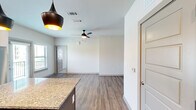 This thoughtfully designed single-floor residence offers a functional and modern layout across five distinct spaces: a kitchen, living room, bedroom, bathroom, and closet. The open-concept kitchen is a standout feature, showcasing rich dark-stained cabinetry, granite countertops, a white subway tile backsplash, and a full suite of stainless steel appliances including a range, microwave, and refrigerator. A central island with a granite surface and stylish pendant lighting anchors the kitchen and flows seamlessly into the living area, which features warm wood-look flooring and a ceiling fan. The living space is bright and clean with crisp white walls and natural light filtering in from nearby windows. The bedroom offers plush carpeting, a window with blinds that brings in natural light, and a calm, neutral palette. An adjacent closet provides dedicated storage. The bathroom is finished with large-format, light-toned tile surrounding a full soaking tub and shower combo, complemented by chrome fixtures. Throughout the space, consistent design choices — including paneled interior doors with brushed hardware and wood-look flooring — create a cohesive, contemporary aesthetic.