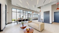Located at 38 Mangum St SW in Atlanta, GA, this rooftop lounge offers a well-appointed, open-plan gathering space designed for both relaxation and social events. The interior is defined by soaring ceilings with sleek linear LED lighting accented by bold orange pendant fixtures, creating a contemporary and energetic ambiance throughout.

The lounge area features a plush cream leather sofa, a patterned geometric area rug, and rounded wood coffee tables, offering a comfortable setting for casual gatherings. A full kitchenette lines one wall, outfitted with light gray shaker-style cabinetry, white quartz countertops, a herringbone tile backsplash, stainless steel appliances including a dishwasher and refrigerator, and a deep undermount sink. A window-side bar counter with tall seating provides additional space for guests.

Floor-to-ceiling black-framed windows and glass doors flood the interior with natural light and frame views of the surrounding Atlanta skyline. These doors open directly onto a rooftop outdoor terrace furnished with seating and string lights, extending the entertaining space outdoors. Polished terrazzo flooring runs throughout, adding a refined, durable finish. A dining table with seating for several guests sits adjacent to the terrace access, ideal for group meals or meetings. The overall design balances modern industrial elements with warm, inviting details.