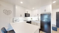 This efficiently laid-out one-bedroom, one-bathroom residence delivers a clean, modern living experience across a single floor. The open-concept design maximizes every square foot, creating a seamless flow between the living area and the kitchen.

The kitchen is a standout feature, outfitted with crisp white shaker cabinetry, matte black hardware, and bright white quartz countertops. Black stainless steel appliances — including a refrigerator, electric range, and over-the-range microwave — provide a bold contrast to the white palette. A subway tile backsplash adds texture, while the peninsula with bar seating offers an inviting spot for casual dining or entertaining.

Light wood-look flooring runs throughout the space, contributing to an airy, cohesive feel. The living area is accessible via a clean hallway entry and benefits from a wall-mounted mini-split system for climate control.

The bedroom is a comfortable retreat, featuring a large window that brings in natural light and an outdoor view, recessed lighting, a wall-mounted mini-split unit, and light, neutral walls that create a calm atmosphere.

The bathroom is finished with a white shaker vanity, quartz countertop, a large mirror with modern lighting, and a walk-in shower adorned with marble-style tile — combining style and function in a compact, well-appointed space.
