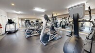 Located at 39 Buckland St in Manchester, Connecticut, this well-equipped fitness center offers a comprehensive workout environment within a single open-plan space. The room features durable dark rubber flooring throughout, providing a practical surface suited for a wide range of exercises. Large wall-mounted mirrors line multiple walls, visually expanding the space and allowing users to monitor their form during workouts.

The cardio equipment selection includes Landice treadmills, elliptical trainers, and stationary bikes — both upright and recumbent — catering to varied fitness routines. A multi-station cable machine and a dedicated free weight area with a full rack of dumbbells and a weight bench address strength training needs. A wall-mounted flat-screen TV is positioned for easy viewing from the cardio machines.

A standout architectural feature is the stacked-stone fireplace with a traditional mantel, adding warmth and a distinctive aesthetic to the room. Natural light filters in through multiple windows with white trim, complementing the bright, recessed, and flush-panel overhead lighting. The clean white walls and neutral design elements create a bright, motivating atmosphere. An emergency exit door provides direct access to the exterior, ensuring convenience and safety for all users.