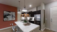 This single-floor residence showcases a thoughtfully designed interior that balances modern aesthetics with functional living. The kitchen serves as the centerpiece of the space, featuring striking dark cabinetry that contrasts beautifully against crisp white quartz countertops and a large central island. The island provides generous workspace and casual seating, illuminated by a pair of stylish industrial-style pendant lights that hang from above. A classic white subway tile backsplash adds texture and brightness to the cooking area, while stainless steel appliances — including a French door refrigerator and a range — lend a polished, contemporary finish. An accent wall painted in a warm terracotta hue adds a bold pop of color and visual depth, complementing the neutral tones throughout the rest of the space. A piece of abstract wall art reinforces the modern character of the interior. Wood-look flooring grounds the space with warmth, tying together the dark and light contrasts found throughout the kitchen and adjoining areas. Recessed lighting overhead, combined with the pendant fixtures, ensures the space is well-lit and inviting. The overall ambiance is contemporary and refined, offering a welcoming environment that is both practical and visually dynamic.
