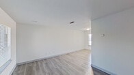 This single-floor space offers a straightforward, well-maintained layout designed for comfortable everyday living. The living area is notably open and bright, featuring light gray wood-look flooring that extends consistently throughout the unit, crisp white walls, and a textured ceiling. Multiple windows fitted with horizontal blinds allow generous natural light to fill the space, creating an airy atmosphere. A subtle platform transition separates areas within the main living zone, adding a mild architectural detail to the otherwise clean-lined interior.

The kitchen is equipped with gray cabinetry on both upper and lower sections, complemented by white countertops and a classic white subway tile backsplash. A stainless steel double-basin sink, black dishwasher, and ample storage make the kitchen both functional and visually cohesive. A window above the counter allows additional natural light into the workspace.

The bathroom features a dual-sink vanity with white countertops and gray cabinetry that matches the kitchen aesthetic. A wall-mounted vanity light, a full tub-shower combination with a white surround, and light wood-look flooring maintain the consistent, clean design found throughout the rest of the unit. Overall, the space presents a neutral, move-in-ready environment with a modern yet understated finish palette.