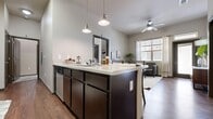 This well-appointed 4-bedroom, 4-bathroom single-story unit offers a thoughtfully designed layout suited for shared or family living. The open-concept kitchen and living area serves as the heart of the home, featuring a central island with a double sink, dark espresso cabinetry, stainless steel appliances including a refrigerator, range, and dishwasher, and warm hardwood-style flooring throughout. Stylish pendant lighting illuminates the kitchen island, while a ceiling fan in the adjacent living area promotes comfortable airflow. Large windows in the living space allow generous natural light to fill the room, creating a bright and welcoming atmosphere.

The four bedrooms are carpeted for comfort and offer a cozy, private feel. Each room features neutral tones and windows that bring in natural light, with some rooms offering views of the surrounding exterior. The bedrooms are efficiently sized, providing practical living space for each occupant.

Each of the four bathrooms is finished consistently with hardwood-style flooring, dark vanity cabinetry with light countertops, a tub-shower combination with tile surround, and overhead storage. Two connecting hallways help facilitate smooth circulation throughout the unit, tying all rooms together in a cohesive, functional floorplan.