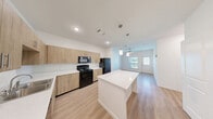 This well-designed 2-bedroom, 3-bathroom single-story unit offers a thoughtfully laid-out floor plan that maximizes functionality. The open-concept kitchen and living area serve as the heart of the home, featuring light wood-tone cabinetry, white quartz countertops, a full suite of black appliances including a gas range, built-in microwave, refrigerator, and dishwasher, and a central kitchen island with pendant lighting above. Light wood-look flooring runs seamlessly throughout the entire unit, creating a cohesive and bright aesthetic. The living area is accented by a ceiling fan and benefits from natural light through a window and glass-panel entry door. Each bedroom is generously proportioned, featuring ceiling fans, large windows with outdoor views, and ample closet space including sliding double-door closets. The bathrooms are finished with warm wood vanities, white countertops, framed mirrors, and built-in open shelving for additional storage. The unit also includes a dedicated closet housing a water heater and washer/dryer connections, adding everyday convenience. Clean white walls, recessed lighting, and consistent finishes throughout lend the space a fresh, modern feel.
