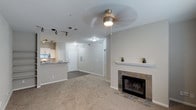 This single-floor residence offers an open and functional layout designed for comfortable everyday living. The living area serves as the central gathering space, finished with soft wall-to-wall carpeting that adds warmth underfoot. A standout feature is the tile-surround fireplace set beneath a classic white wood mantel, providing both a visual focal point and a cozy atmosphere. A ceiling fan with an integrated light fixture keeps the space well-ventilated and illuminated.

The living area flows seamlessly into the kitchen, which is distinguished by its track lighting system mounted along the ceiling—ideal for task-focused illumination. The kitchen features granite countertops, light-toned cabinetry, and stainless steel appliances including a microwave, giving it a clean, modern feel. A raised breakfast bar separates the kitchen from the living space while maintaining an open sightline throughout.

Hard surface flooring near the entryway transitions to carpet in the main living area, creating a clear delineation between zones. The neutral color palette of warm whites and soft grays throughout contributes to a bright, cohesive aesthetic that feels move-in ready and versatile.