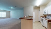 This single-floor residence is designed with an open, functional layout that connects the kitchen and living areas seamlessly. The kitchen serves as a central hub, featuring a peninsula with a dark granite-style countertop, an integrated sink, and white cabinetry that extends to the ceiling, offering generous storage. White appliances, including an electric range and over-the-range microwave, complement the clean aesthetic. Tile flooring runs throughout the kitchen, transitioning to plush carpet in the adjoining living area, which provides a comfortable and spacious setting with neutral-toned walls.

The bedrooms are carpeted and bathed in natural light through windows fitted with blinds that frame views of surrounding greenery. Each room offers a clean, understated design with ample wall space and closet access, including a louvered-door closet visible in one of the larger rooms.

The bathroom is well-appointed with a white vanity featuring dark granite-style countertops, a single sink, and ample cabinet storage below. A full tub and shower combination with tiled surround occupies one end of the room, finished with warm tile flooring throughout. Overall, the unit maintains a consistent neutral palette, creating a cohesive and move-in ready atmosphere.