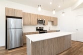 This well-designed 2-bedroom, 3-bathroom residence in Idaho Falls, Idaho offers a thoughtful single-floor layout with modern finishes throughout. The open-concept kitchen and living area serves as the heart of the home, featuring warm-toned wood cabinetry, white quartz countertops, stainless steel appliances including a refrigerator, range, microwave, and dishwasher, and a kitchen island with pendant lighting overhead. Light wood-style flooring flows through the main living areas, enhancing the bright, airy feel of the space. The living room is generously proportioned with recessed lighting, tall ceilings, and a sliding glass door that opens to a private balcony with outdoor views. Both bedrooms are carpeted and well-sized, with the primary bedroom offering a tray ceiling detail and ample closet space. The three bathrooms are finished consistently with wood-tone vanity cabinetry, white countertops, and wood-style flooring. The full bathrooms include a tub-shower combination, while all feature large mirrors and brushed nickel hardware. A hallway connects the private areas of the home, and a stacked laundry unit is conveniently located within the unit. The overall aesthetic is clean, contemporary, and move-in ready.