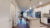 This single-floor residence offers a thoughtfully designed open-concept layout that seamlessly connects the kitchen, dining, and living areas. The kitchen is a standout feature, anchored by a large granite-topped island with an undermount sink, pendant lighting, white shaker cabinetry, a subway tile backsplash, and stainless steel appliances. Rich hardwood-style flooring runs throughout the main living areas, adding warmth and continuity to the space.

The living room is bright and inviting, with floor-to-ceiling French doors that flood the room with natural light and provide access to the outdoors. A ceiling fan overhead and generous wall space contribute to the room's comfortable, airy feel.

The primary bedroom is carpeted and generously proportioned, accompanied by an en-suite bathroom that includes a granite-topped double vanity with white cabinetry, a glass-enclosed walk-in shower with white tile surround, and hardwood-style flooring. A spacious walk-in closet with wire shelving and hanging rods provides ample storage. The second bedroom is equally comfortable, served by a well-appointed bathroom featuring a granite vanity, white cabinetry, and a shower-tub combination. A washer unit is also present within the unit, adding everyday convenience to this polished and functional home.