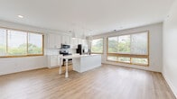 Located at 1115 Seigle Ave in Charlotte's dynamic 28205 zip code, this single-floor residence offers a clean, modern aesthetic throughout. The open-concept living and kitchen area serves as the heart of the home, anchored by a central island with pendant lighting and a sleek undermount sink. White shaker cabinetry, white subway tile backsplash, light countertops, and a full suite of stainless steel appliances complete the kitchen. Warm-toned wood-look flooring runs seamlessly throughout the entire space, complementing the crisp white walls. Multiple wood-framed windows flood the living and kitchen areas with natural light and offer pleasant views of surrounding greenery. The bedrooms are bright and well-proportioned, with generous double-door closets providing ample storage. The bathrooms are tastefully finished, featuring white shaker vanities with dark countertops — one bath includes a tiled tub-shower combination with matte black fixtures, while another offers a walk-in glass shower. A dedicated laundry area houses a full-size front-loading washer and dryer. A well-lit hallway with track lighting connects the private areas of the home, creating a functional and cohesive layout throughout.