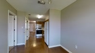 This single-floor residence offers a practical and comfortable layout designed for easy living. The space is anchored by rich, dark hardwood flooring that runs throughout, lending warmth and a cohesive feel to the interior. A central hallway serves as the main artery of the home, connecting the various living spaces and providing a clear sense of flow from one area to the next.

The kitchen is a standout feature, outfitted with warm wood cabinetry, a white electric range, a full-size refrigerator, and an overhead range hood. The cabinetry provides ample storage, while the compact yet efficient layout makes the most of the available space. Neutral gray walls throughout the residence create a clean, understated backdrop that complements both the flooring and cabinetry tones.

Ceiling-mounted light fixtures provide consistent illumination across the hallway and kitchen areas, ensuring the space remains bright and functional. HVAC vents are thoughtfully positioned in the ceiling for even climate control throughout. White panel doors and crisp white baseboards add a classic finishing touch, contributing to the overall tidy and well-maintained character of the space. The layout is straightforward and accessible, making this a highly functional single-floor residence.
