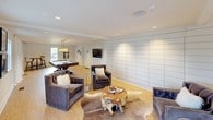 The Avia Clubhouse is a thoughtfully designed single-floor community space that seamlessly blends comfort, style, and functionality. The bright and welcoming lounge area features light hardwood flooring, large windows that flood the room with natural light, and a sophisticated seating arrangement of cream sofas and teal accent chairs centered around a geometric patterned rug. A contemporary multi-arm chandelier adds an elegant focal point overhead.

Adjacent to the lounge, the game room offers a relaxed, social atmosphere anchored by a full-size billiards table and plush velvet lounge chairs arranged around a rustic live-edge wood coffee table. Shiplap-style wall paneling lends a clean, modern-coastal aesthetic, complemented by a wall-mounted flat-screen television for added entertainment.

The kitchenette and bar area serves as the social hub of the clubhouse, featuring a generous white quartz island with gold wire barstools. A vivid teal mosaic tile backsplash frames open shelving and brass accent lighting, creating a striking visual backdrop. The space is equipped with a coffee station, beverage refrigerator, and ample cabinetry. French doors throughout the clubhouse invite views of the outdoors, reinforcing an open, airy ambiance. The overall design reflects a refined yet approachable aesthetic ideal for community gatherings.