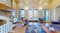 Located at 3131 Simpson Stuart Rd in Dallas, TX, this single-floor community clubhouse offers a thoughtfully designed gathering space that balances comfort and functionality. The living room serves as the heart of the space, showcasing a dramatic floor-to-ceiling stone fireplace with a wood mantle as its centerpiece. Soaring vaulted ceilings amplify the sense of openness, while warm wall sconces and carefully selected artwork contribute to an inviting ambiance. Large windows and French doors flood the area with natural light and provide views of the surrounding exterior, while tile flooring laid in a classic diamond pattern runs throughout. A geometric-patterned area rug anchors the seating area, complementing the space's blue and gold color accents. Coffered ceiling details add architectural depth to the entryway, which connects seamlessly to the main living area via French doors. Two kitchens support the space's event and community use, each outfitted with stainless steel sinks, ample cabinetry, countertop appliances, and good natural light from windowed walls. The overall design is polished yet approachable, making this clubhouse a versatile venue for community gatherings and everyday resident use.