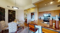 This single-floor residence offers a thoughtfully designed layout that balances comfort and functionality throughout. The living room is a standout space, characterized by soaring vaulted ceilings, plush carpeting, and a ceiling fan that enhances the airy atmosphere. A sliding glass door opens directly onto a private balcony, flooding the room with natural light and offering expansive panoramic views of the surrounding landscape. A built-in arched niche adds architectural character, while the open layout provides generous room to relax and entertain.

The kitchen is efficiently arranged in a galley style, featuring warm wood cabinetry, stone-toned countertops, and a full suite of black appliances including a refrigerator, electric range, dishwasher, and built-in microwave. An adjacent dining area with a breakfast bar and pendant lighting creates a natural flow between cooking and dining spaces. A dedicated in-unit laundry closet nearby adds everyday convenience.

The bedroom is a serene retreat, appointed with plush carpeting, a ceiling fan, and a large window framing scenic outdoor views. Warm neutral tones and ample space contribute to a restful ambiance. The full bathroom features hardwood-style flooring, a tub-shower combination with decorative tile accents, and a wood-toned vanity with ample storage.