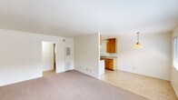 This well-organized single-floor unit offers a straightforward and efficient layout comprising a living room, bedroom, kitchen, bathroom, and hallway. The living room is a bright, open space featuring neutral carpet flooring, white walls, and a large window that allows ample natural light to flow in. A wall-mounted HVAC unit provides climate control, and tile flooring at the entryway transitions seamlessly into the carpet. The kitchen is positioned adjacent to the living area and features warm-toned wooden cabinetry — both upper and lower — offering generous storage. A double stainless steel sink, granite-style laminate countertops, and a gas range make the kitchen highly functional. Tile flooring runs throughout the kitchen for easy maintenance. The bedroom is a comfortable, carpeted room with a window overlooking the outdoors, a flush-mount ceiling light, and clean white walls that create a calm atmosphere. The bathroom is finished with white tile surrounding the tub and shower combination, complemented by a single vanity with a mirror, and a window that provides ventilation and natural light. A hallway connects the main rooms, completing this efficient and move-in ready layout.