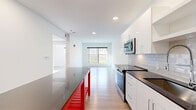 Located at 343 Mt Support Rd in Lebanon, NH, this thoughtfully designed one-bedroom, one-bathroom unit offers a clean, modern aesthetic across a single floor. The open-concept living and kitchen area is bright and airy, anchored by recessed lighting and light-toned hardwood flooring throughout. The kitchen is well-appointed with white shaker-style cabinetry, dark countertops, a subway tile backsplash, and a full suite of stainless steel appliances including a range, microwave, and refrigerator. A bold red kitchen island with a dark countertop adds a striking visual element and extra prep space. The living area features a large window that frames views of the surrounding wooded landscape, filling the space with natural light. The bedroom is comfortably sized with dual windows overlooking the trees, providing a peaceful, nature-filled backdrop. A walk-in closet with wire shelving offers generous storage. The bathroom is finished with white cabinetry, a dark-topped vanity, a large mirror, and a glass-enclosed shower. Additional conveniences include in-unit laundry, a utility room, hallway storage, and a dedicated closet, making this a highly functional and well-organized living space.