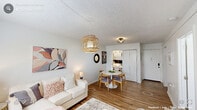 Located at 500 E Hargett St in the heart of downtown Raleigh, NC, this one-bedroom, one-bathroom residence offers a well-planned single-floor layout that maximizes every square foot. Warm hardwood-style flooring flows consistently throughout the unit, lending a cohesive and inviting feel to the entire space.

The living room features soft blue-gray walls, a woven pendant light fixture, and a window dressed with sheer curtains that allow natural light to filter in. Adjacent to the living area, the dining space accommodates a round table and chairs beneath an industrial-style globe pendant light, with a view into the bedroom beyond.

The kitchen is efficiently designed with bamboo countertops, open shelving, and a striking white herringbone tile backsplash. A stainless steel sink and clean white walls give the space a crisp, modern character.

The bedroom is a comfortable retreat featuring a window with natural light, a textured accent wall in cool gray, and a closet with direct access to the bathroom. The bathroom is clean and functional, outfitted with white subway tile surrounding the tub-shower combo, a white vanity with a wood-topped shelf, and warm lighting. Throughout the unit, the design is cohesive, modern, and thoughtfully detailed.