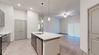 Located at Lakewood Ranch Boulevard in Sarasota, Florida, this single-floor residence offers three bedrooms and three bathrooms within a thoughtfully designed layout. The open-concept living and kitchen area serves as the heart of the home, anchored by a large central island with a white quartz countertop, undermount sink, and stylish pendant lighting. The kitchen is appointed with dark wood cabinetry, stainless steel appliances, a tile mosaic backsplash, and recessed lighting that illuminates the space effectively. Light wood-style flooring flows through the main living areas, complemented by tall ceilings that enhance the sense of openness. The living room features a ceiling fan and access to a sliding glass door with vertical blinds. The bedrooms are carpeted for comfort and receive natural light through slatted window blinds. Each bedroom is served by its own bathroom, and the closets are outfitted with multi-tier wire shelving systems offering generous storage. The bathrooms feature large-format tile flooring, wood-toned floating vanities with quartz countertops, backlit mirrors, and soaking tubs with tile surrounds. The clean, neutral palette and modern finishes throughout give this residence a cohesive and contemporary character.