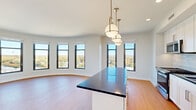 This thoughtfully designed residence offers five bedrooms and two bathrooms across a single floor, combining modern finishes with a functional, open layout. The heart of the home is a striking open-concept kitchen and living area. The kitchen is outfitted with white shaker cabinetry, dark countertops, a white subway tile backsplash, stainless steel appliances, and a central island with pendant globe lighting suspended from brass fixtures — creating an elegant focal point. The living area features a distinctive curved wall lined with large black-framed windows that flood the space with natural light and frame sweeping treetop and neighborhood views. Warm-toned hardwood flooring flows consistently throughout the unit. The five bedrooms are well-proportioned, with the primary bedroom offering generous space and natural light through dual windows. Each bedroom includes built-in closet storage with clean white panel doors. The two bathrooms are finished with white subway tile, classic mosaic dot flooring, marble-style vanity tops, and white cabinetry. One bathroom features a full tub-shower combination, while the other offers a frameless glass walk-in shower. The overall ambiance is bright, clean, and contemporary.