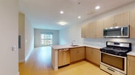 This single-floor residence offers a clean, contemporary design throughout. The open-concept layout seamlessly connects the kitchen and living area, creating a spacious and functional flow. Light wood-toned flooring runs throughout the main living spaces, complementing the neutral wall tones and contributing to a bright, airy atmosphere.

The kitchen is well-appointed with light wood cabinetry, granite stone countertops, and a full suite of stainless steel appliances, including a gas range, over-the-range microwave, dishwasher, and refrigerator. A peninsula with additional counter space enhances both prep area and casual dining options. Recessed lighting illuminates the kitchen efficiently.

The living area is generously proportioned, benefiting from a large window that invites natural light and provides views of the surrounding exterior. The open floor plan allows for flexible furniture arrangements to suit a variety of lifestyles.

The bathroom is finished to a high standard, featuring large-format neutral tile surrounding a soaking tub with an overhead shower. A single-basin vanity with wood cabinetry and a wide mirror with coordinating light fixtures completes the space with a polished, modern aesthetic.

Overall, the unit presents a cohesive, modern design with quality finishes, practical layouts, and abundant natural light throughout.