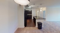 This single-floor residence offers a thoughtfully designed layout that balances open communal spaces with comfortable private quarters. The kitchen serves as a central highlight, showcasing rich dark cabinetry, dark granite countertops, a tiled backsplash, and black appliances including a refrigerator, range, and microwave. A peninsula with pendant lighting above provides additional prep and seating space, flowing seamlessly into the open living area. The living room is finished with plush neutral carpeting and a ceiling fan with integrated lighting, creating a comfortable, functional atmosphere. The transition between the kitchen's hardwood-style flooring and the living area's carpet is a clean and defining architectural detail. The bedrooms are generously proportioned, each featuring soft carpeting, ceiling fans, and windows with blinds that allow natural light to filter in. One bedroom includes an adjacent walk-in closet, offering notable storage capacity. Both bathrooms are consistently finished with light tile flooring, dark vanity cabinetry, light countertops, and full tub-shower combinations fitted with brushed nickel fixtures. The overall design palette of neutral tones, dark wood accents, and clean white trim creates a cohesive and modern aesthetic throughout the space.