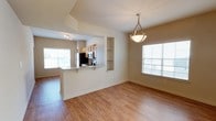This two-story residence offers a thoughtfully designed open-concept main level where the kitchen and living/dining areas flow seamlessly together. The kitchen is anchored by a peninsula with a granite-style countertop that provides bar-style seating, making it a natural gathering point. Dark-finished cabinetry, stainless steel appliances, and a built-in microwave equip the kitchen for everyday functionality. Flanking the peninsula, a set of open display shelves adds architectural interest while offering storage or decorative space.

The adjacent dining and living areas are bathed in natural light, courtesy of multiple windows dressed with horizontal blinds. An elegant pendant light fixture hangs overhead, adding a refined focal point to the dining space. Warm-toned hardwood-style flooring runs throughout the main level, contributing to a cohesive and inviting ambiance.

Vaulted or elevated ceiling details near the kitchen add visual depth and an airy quality to the space. The neutral wall tones throughout create a versatile backdrop, complementing the warm flooring and dark cabinetry. The second floor provides additional living space, extending the overall functionality of this well-appointed home.