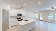 This well-appointed two-story home in Augusta, GA offers 3 bedrooms and 4 bathrooms across two thoughtfully designed floors. The main level features an open-concept kitchen and living area bathed in natural light from multiple windows. The kitchen is outfitted with crisp white shaker cabinets, white quartz countertops, stainless steel appliances including a range, microwave, and refrigerator, a tile backsplash, and a central island with an undermount sink — ideal for both cooking and entertaining. The living room extends naturally from the kitchen, featuring light wood-look flooring, a ceiling fan, and a rear door providing outdoor access. A staircase with blue-painted treads and a wood handrail connects the floors. Upstairs, the primary bedroom includes a ceiling fan and a walk-in closet with wire shelving, accompanied by an en-suite bathroom featuring a white vanity, quartz countertop, framed mirror, and a glass-enclosed walk-in shower. Two additional bedrooms and multiple closets provide generous storage. A dedicated laundry room houses a full-size washer and dryer. The attached garage with an automatic opener rounds out the functional layout. Light wood-look flooring and a neutral palette carry throughout, lending the home a clean, modern aesthetic.