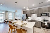 Located at 1350 Dresden Dr NE in Brookhaven, GA, this well-appointed one-bedroom, one-bathroom residence offers a thoughtfully designed open-concept layout across a single floor. Light hardwood-style flooring flows throughout the main living areas, creating a cohesive and contemporary aesthetic.

The kitchen is a functional centerpiece, featuring sleek wood-toned cabinetry, a white subway tile backsplash, stainless steel appliances — including a full-size refrigerator, dishwasher, microwave, and range — and a white quartz-topped island with seating for two, illuminated by modern pendant lights. The kitchen flows seamlessly into the living room, which is bathed in natural light from large windows with views to the outdoors and a sliding glass door that opens to a private balcony.

The bedroom is a standout space, highlighted by a bold teal geometric accent wall that adds a striking design element. It features plush carpeting, a ceiling fan, and a window that brings in additional natural light. Direct access to the full bathroom provides added convenience. The bathroom is clean and modern, with wood-toned cabinetry, a white countertop vanity, and light flooring. A dedicated closet completes the unit's layout.