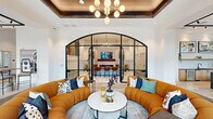Located at 1821 Chatham Flats Dr in Apex, NC, this single-floor community amenity space offers a generously sized, thoughtfully curated environment designed for both socializing and productivity. The entry foyer welcomes visitors with floor-to-ceiling black-framed glass doors and windows that flood the space with natural light and offer views of the surrounding landscaping and greenery.

The main lounge area is an architectural centerpiece, featuring a dramatic arched black steel and glass partition that frames an inner gathering room. A coffered wood-paneled ceiling overhead is adorned with a sculptural globe chandelier, adding warmth and elegance. Adjacent to the lounge, a second seating area boasts soaring ceilings, a sleek linear fireplace set into a white brick accent wall, a wall-mounted display, and curated artwork throughout.

The dining area is anchored by bold floor-to-ceiling windows that bring in abundant natural light and outdoor views. A bar-style kitchen features a large island with dark countertops, light wood cabinetry, pendant lighting, and bar seating with plush blue velvet stools. A dedicated private office provides an intimate meeting setting with a conference table and wall-mounted display. Hallways adorned with framed artwork connect each area, creating a cohesive, gallery-like flow throughout the space.