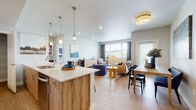 This thoughtfully designed single-floor residence offers a seamless open-concept layout connecting the kitchen, dining, and living areas into one bright, cohesive space. The kitchen is outfitted with stainless steel appliances, sleek quartz countertops, wood-tone cabinetry, pendant lighting over the island, and a dedicated walk-in pantry with built-in shelving for ample storage. Light wood-style flooring flows throughout the main living areas, enhancing the airy, modern feel. The living room enjoys generous natural light from multiple windows with views of the surrounding neighborhood, complemented by recessed lighting and flush-mount fixtures overhead. A dedicated dining area sits adjacent to the living space, ideal for everyday meals or entertaining. Both bedrooms feature plush carpeting, ceiling fans or overhead lighting, and large windows that invite natural light. The full bathroom includes a wood-tone vanity with quartz countertops, a soaking tub with shower, and light tile flooring. A hallway connects the private areas of the residence and includes an in-unit laundry closet with a stacked washer and dryer. The overall ambiance is clean, contemporary, and welcoming throughout.