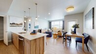 This thoughtfully designed single-floor residence offers a seamless open-concept layout connecting the kitchen, dining, and living areas into one bright, cohesive space. The kitchen is outfitted with stainless steel appliances, sleek quartz countertops, wood-tone cabinetry, pendant lighting over the island, and a dedicated walk-in pantry with built-in shelving for ample storage. Light wood-style flooring flows throughout the main living areas, enhancing the airy, modern feel. The living room enjoys generous natural light from multiple windows with views of the surrounding neighborhood, complemented by recessed lighting and flush-mount fixtures overhead. A dedicated dining area sits adjacent to the living space, ideal for everyday meals or entertaining. Both bedrooms feature plush carpeting, ceiling fans or overhead lighting, and large windows that invite natural light. The full bathroom includes a wood-tone vanity with quartz countertops, a soaking tub with shower, and light tile flooring. A hallway connects the private areas of the residence and includes an in-unit laundry closet with a stacked washer and dryer. The overall ambiance is clean, contemporary, and welcoming throughout.