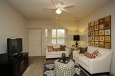 This single-floor residence offers a thoughtfully designed layout that balances comfort and functionality across its key living areas. The kitchen is equipped with white cabinetry extending to the ceiling, providing ample storage space. It features an electric range, a built-in microwave, a dishwasher, a full-size refrigerator, and a double sink, all set against light tile flooring and neutral countertops. A dedicated dining area with a granite-topped table sits adjacent to the kitchen, which also connects conveniently to an in-unit laundry room. The living room is warm and inviting, finished with carpet flooring and illuminated by a ceiling fan with a light fixture. A front-facing window dressed with blinds allows natural light to fill the space, complemented by a front entry door. The bedroom is generously proportioned, featuring plush carpet, a ceiling fan, and a window overlooking the exterior. The bathroom is finished with patterned wallcovering and tile flooring, and includes a vanity with under-sink storage, a large mirror with vanity lighting, and a toilet. Throughout the residence, neutral tones and consistent finishes create a cohesive and comfortable living environment.