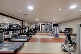 Located at 4200 North Carlin Springs Road in Arlington, VA, this fitness center offers a comprehensive workout facility designed to accommodate a variety of exercise routines. The space spans a generous single floor, providing ample room for both cardio and strength training activities without feeling cramped.

The layout is thoughtfully organized, with a dedicated cardio zone featuring multiple treadmills, elliptical trainers, and stationary bikes from Life Fitness — all positioned for comfortable use. Strategically placed large mirrors along the walls visually expand the space and allow users to monitor their form during workouts.

The strength training area is well-stocked with a selection of selectorized cable and resistance machines, a flat utility bench, and a dumbbell rack with a full range of free weights. A stability ball rounds out the functional fitness offerings. A wall-mounted flat-screen television adds an entertainment element to the space.

The flooring features a distinctive two-tone rubber surface in alternating red and beige stripes, providing both durability and traction. Recessed ceiling lighting delivers consistent, even illumination throughout the room. Near the entrance, a water fountain station and decorative wall art contribute a welcoming touch. The overall ambiance is clean, professional, and conducive to focused, effective exercise.