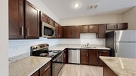 This single-floor residence offers a thoughtfully designed layout across three bedrooms, two bathrooms, a kitchen, hallway, and two closets. Light wood-style flooring flows consistently throughout the living areas and bedrooms, contributing to a cohesive and airy aesthetic.

The kitchen is a standout feature, equipped with rich dark-brown cabinetry, granite-style countertops, a white subway tile backsplash, and a full suite of stainless steel appliances including a range, microwave, dishwasher, and refrigerator. A central island provides additional prep and storage space, while the open sightlines connect the kitchen to the main living area.

The primary bedroom is generously sized and benefits from large sliding glass doors that allow abundant natural light, complemented by a ceiling fan. The additional bedrooms are well-proportioned, each with ceiling fans and windows providing natural light.

Both bathrooms feature dark cabinetry with granite-style countertops and light tile flooring. The primary bathroom includes a glass-enclosed walk-in shower with subway tile surround, while the second bathroom offers a clean, functional layout. Two closets, fitted with wire shelving systems, provide practical storage solutions throughout the residence.