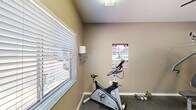 Located at 4260 SE 10th Pl in Gainesville, Florida, this fitness center offers a well-organized exercise space designed to support a variety of workout routines. The room features durable speckled rubber flooring throughout, providing a safe and practical surface for physical activity. Warm taupe-toned walls and overhead fluorescent lighting create a clean, focused environment, while a ceiling fan promotes air circulation during workouts.

The space is equipped with an array of cardio machines, including stationary bikes and elliptical trainers, as well as a multi-station cable weight machine suitable for a range of strength-training exercises. Free weights and additional fitness accessories are also available. A large wall-mounted mirror expands the sense of space and allows users to monitor their form during exercise.

A window with horizontal blinds allows natural light to filter into the room, and a French-style glass door provides access to the space, contributing to an open feel. Posted fitness center rules are clearly displayed, outlining guidelines for safe and responsible use of the facility. Compact yet efficiently arranged, this fitness center delivers essential amenities for residents seeking a convenient on-site exercise option.