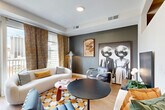 Located at 1557 Logan Street in Denver's Capitol Hill neighborhood, this single-floor studio offers a compact yet efficiently organized layout comprising an open kitchen and living area, a connecting hallway, and a full bathroom. The living room makes a bold design statement with dark slate-gray accent walls, large windows adorned with patterned ochre drapery, and sweeping city views of the Denver skyline. Light hardwood flooring runs throughout, anchoring the eclectic, retro-modern aesthetic. The kitchen is outfitted with sleek, navy-blue cabinetry accented by gold hardware, white subway tile backsplash, a stainless steel gas range, built-in microwave, and a full-size refrigerator — all complemented by a bright window that floods the space with natural light. The hallway connects the living area to the rest of the unit with clean white paneled doors and a patterned runner. The bathroom features a dark, floor-to-ceiling vanity with gold hardware, a glass-enclosed shower, and light hardwood-style flooring — finished with tasteful black-and-white framed artwork. This Denver studio combines thoughtful design details with urban convenience in a compact, well-curated space.