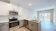 Located in Rochester, MN, this well-designed one-bedroom, two-bathroom unit at Hearthstone Ct NW offers a thoughtful layout with modern finishes throughout. The open-concept kitchen and living area serves as the heart of the home, showcasing two-tone cabinetry with crisp white upper cabinets and gray lower cabinets, complemented by sleek quartz countertops and a full suite of stainless steel appliances including a refrigerator, electric range, over-the-range microwave, and dishwasher. Light wood-look flooring flows seamlessly through the main living area, which opens to a private balcony through sliding glass doors, filling the space with natural light. The bedroom features soft carpet, a large window with exterior views, and direct access to one of the two bathrooms. A dedicated closet space with wire shelving provides ample storage. The second bathroom is well-appointed with gray vanity cabinetry, quartz counters, a tub/shower combo, and matching wood-look flooring. A separate utility/laundry area with built-in shelving adds functional convenience. Clean neutral tones and black hardware accents tie the contemporary aesthetic together throughout the unit.
