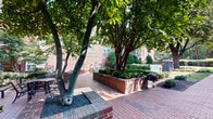 The Manor House Apartment Courtyard in Alexandria, VA is a well-maintained outdoor communal space that combines classic architectural character with thoughtfully designed landscaping. The courtyard is framed by a traditional multi-story red brick building, whose timeless facade sets a refined tone for the entire grounds.

Brick-paved pathways wind throughout the space, connecting various areas of the courtyard and lending a cohesive, polished look underfoot. Mature shade trees provide generous canopy cover, creating cool, dappled areas ideal for outdoor gatherings or quiet relaxation. Ornamental crape myrtles add seasonal color and visual interest throughout the grounds.

Meticulously trimmed hedges and sculpted shrubs are positioned throughout the landscape, reflecting careful and consistent maintenance. Raised brick planter beds introduce additional layers of greenery, while ground-level plantings of ornamental grasses and flowering perennials add texture and variety along building borders.

Classic black lantern-style light posts are placed at regular intervals along the walkways, providing both functional illumination and a charming, traditional aesthetic. A charcoal grill is available within the courtyard area, offering a practical amenity for outdoor cooking. Lush, well-kept lawns surround the building's perimeter, completing the verdant setting. The overall ambiance is inviting, serene, and characteristic of Alexandria's historic neighborhood charm.